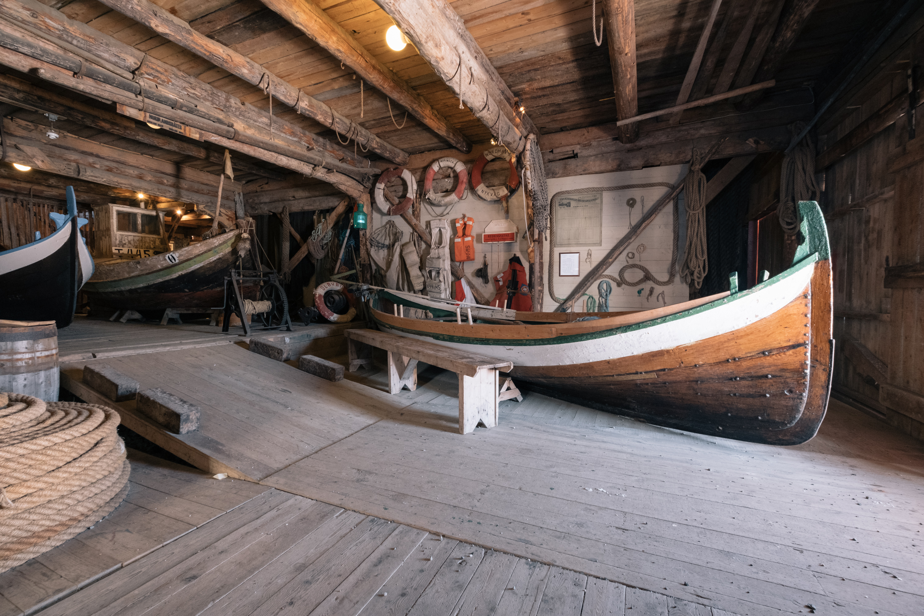 Ein altes Holzboot in einem hölzernenden Hangar. Im Hintergrund stehen weitere Boote